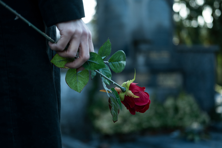 kobieta z czerwoną różą stojąca przy grobie